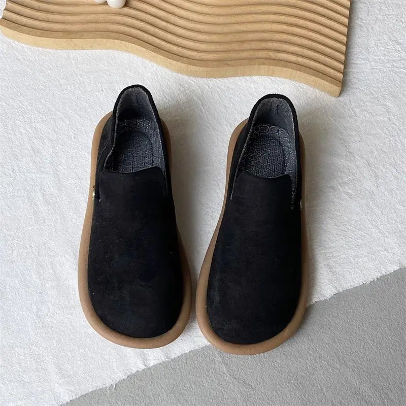 Schwarze Veloursleder-Slipper im Vintage-British-Stil mit niedrigem Absatz mit einer braun wirkenden Gummisohle, von der Rückseite dargestellt.