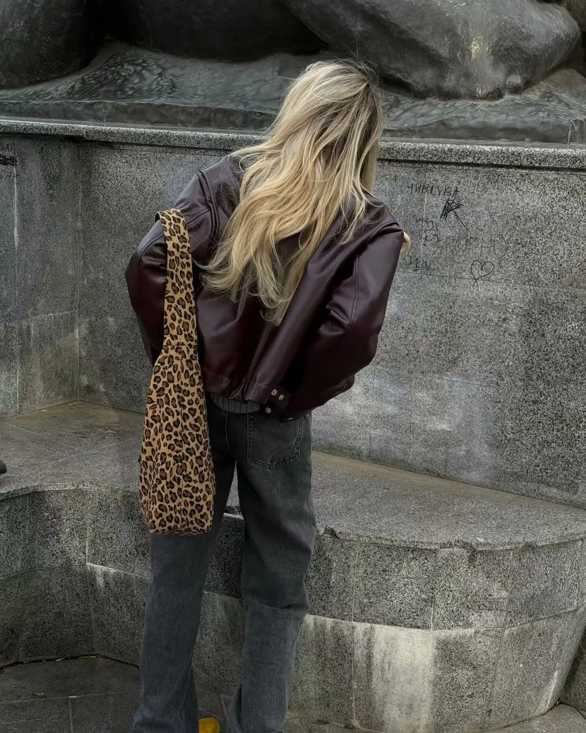 Eine Shopper-Tasche mit Leopardenmuster, mit weicher Textilstruktur sowie kräftigen braunen und beigen Farbflecken, kombiniert mit einer Kunstleder-Bomberjacke mit lockerer Passform, kurz geschnitten im Moto-Stil