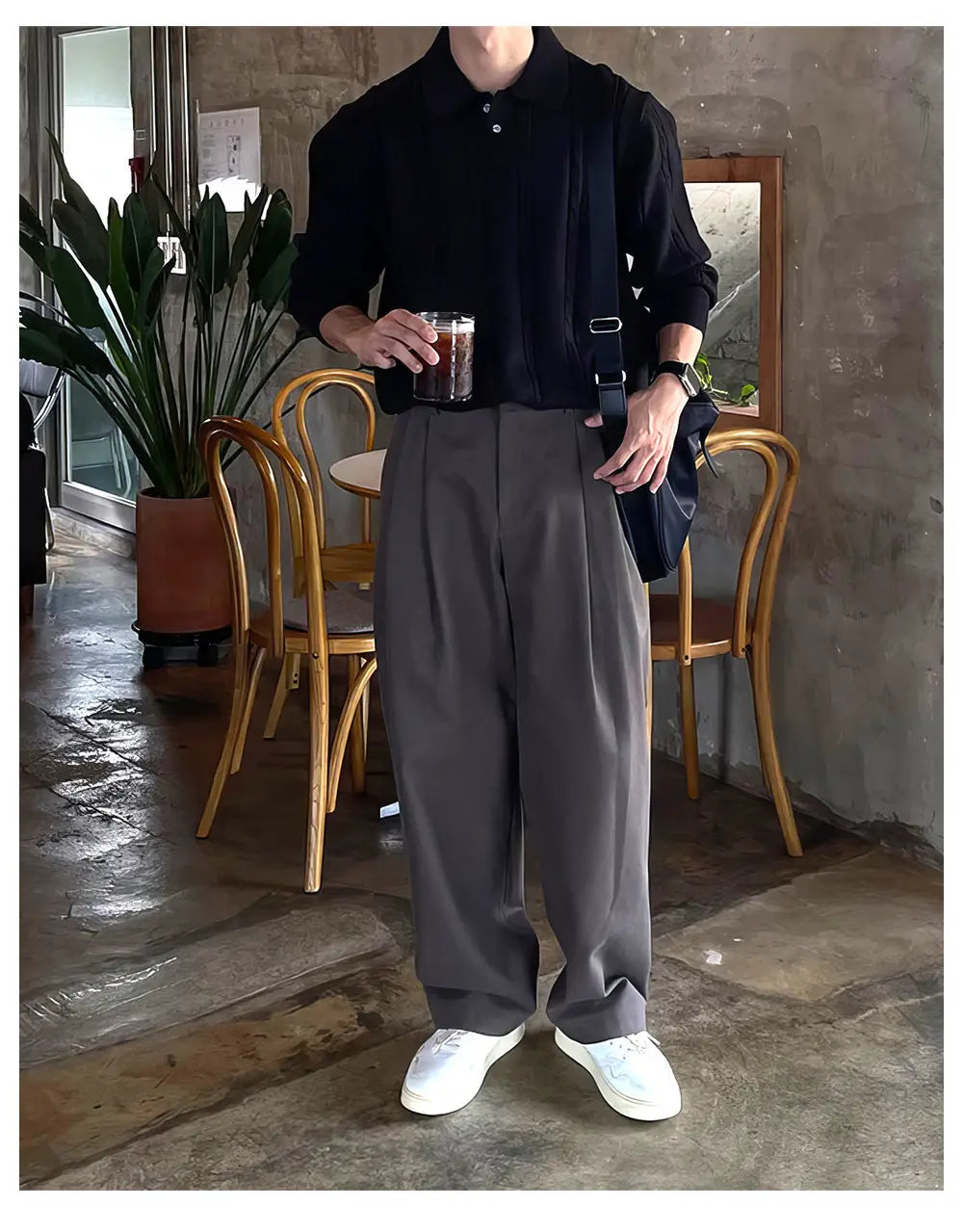 Polo negro de manga larga con cuello abotonado y textura sutil, combinado con pantalones de vestir anchos plisados color gris oscuro para hombre