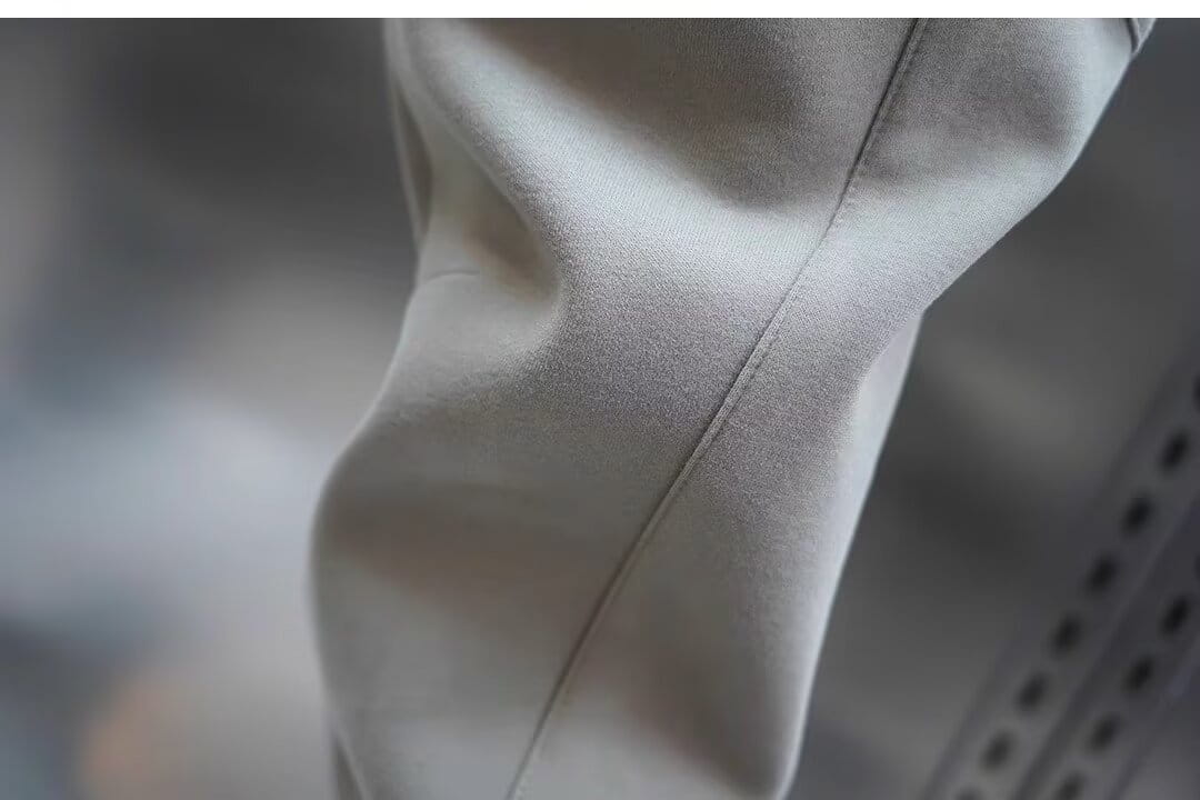 A close-up of light gray men’s casual solid color sweatpants fabric with a soft texture and subtle vertical stitching along the seam.