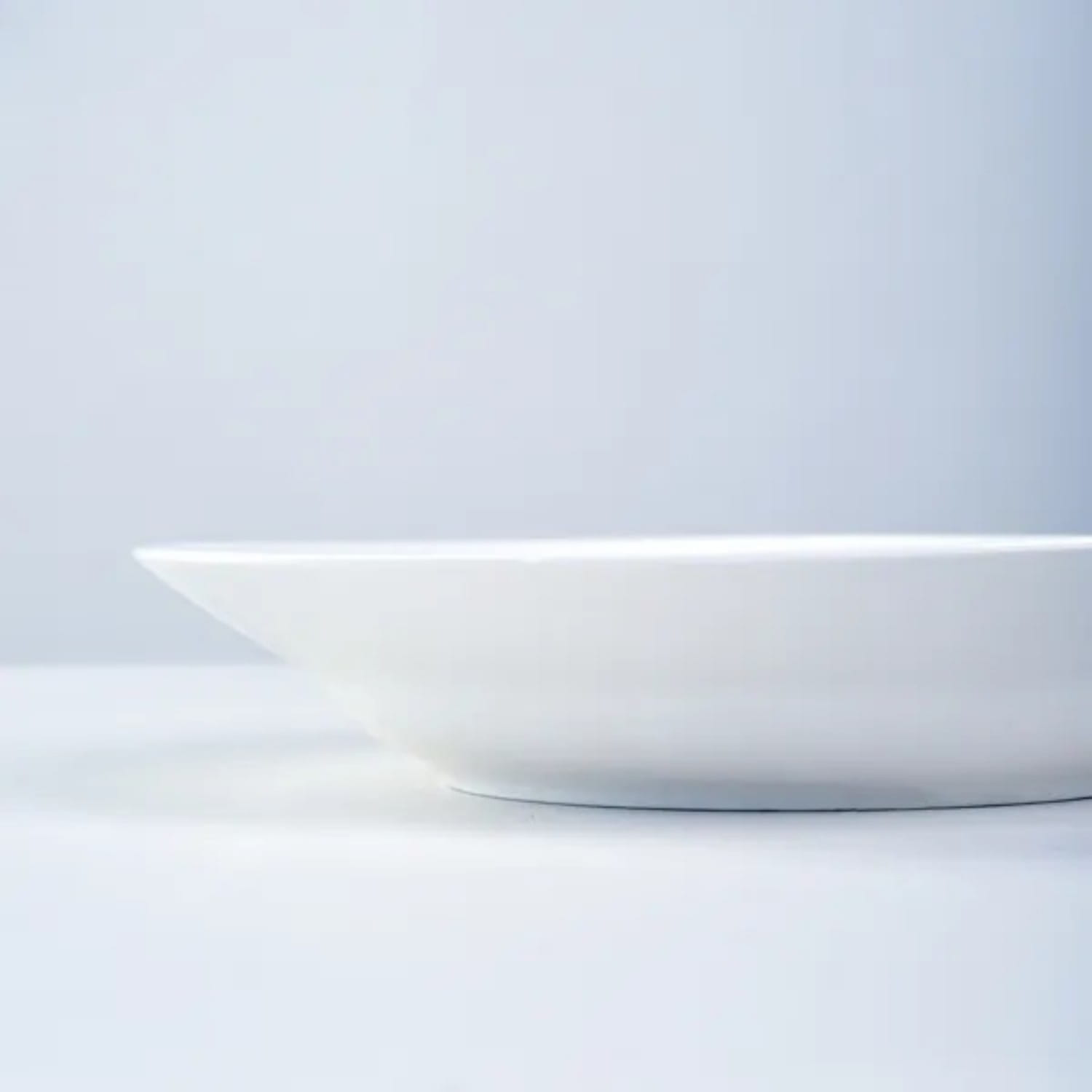 A minimalist white ceramic dinner plate with a smooth glossy finish and subtly curved edges from a set of six 9.5 inch bowls.
