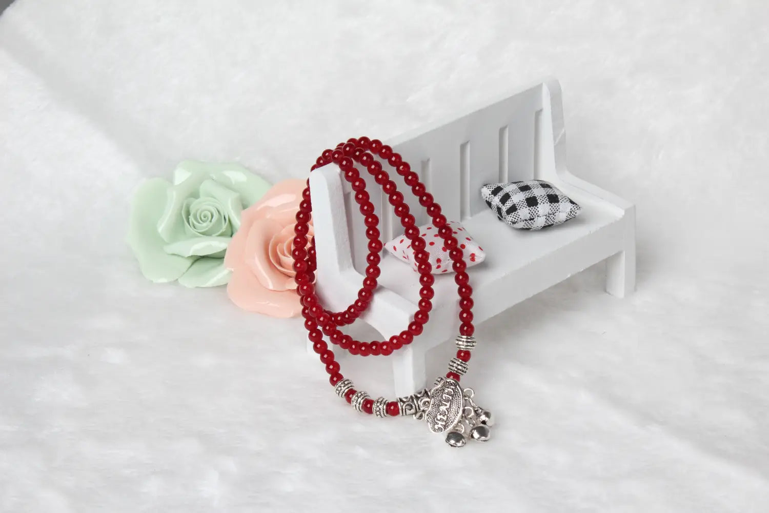 A red agate good luck bracelet with silver-toned engraved protect charm and beads resting on a miniature white bench.