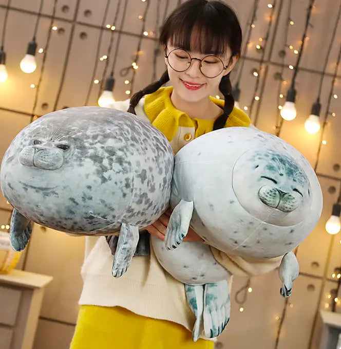 Zwei große gesprenkelte Robben-Plüschtiere mit jeweils einer grauen Variante mit dunklen Flecken und einer weißen Variante mit hellblauen Markierungen aus weichem Material, ideal als Tierkissen.
