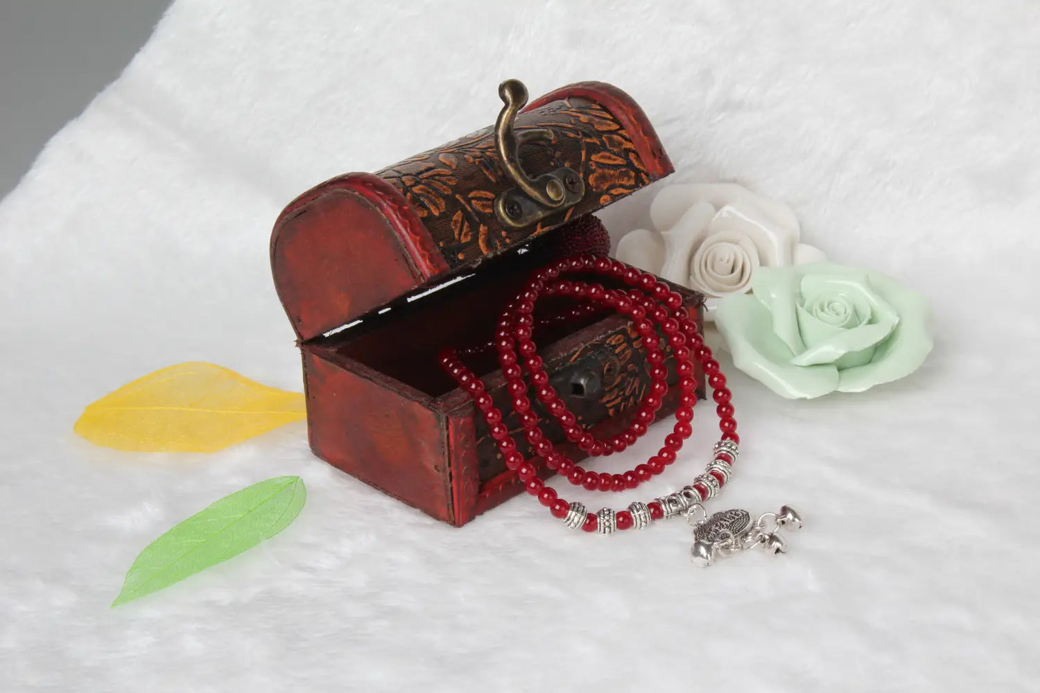 red leather treasure chest with gold-toned metal clasp and floral embossing containing a red agate good luck bracelet with engraved protect charm and matching red beaded necklace