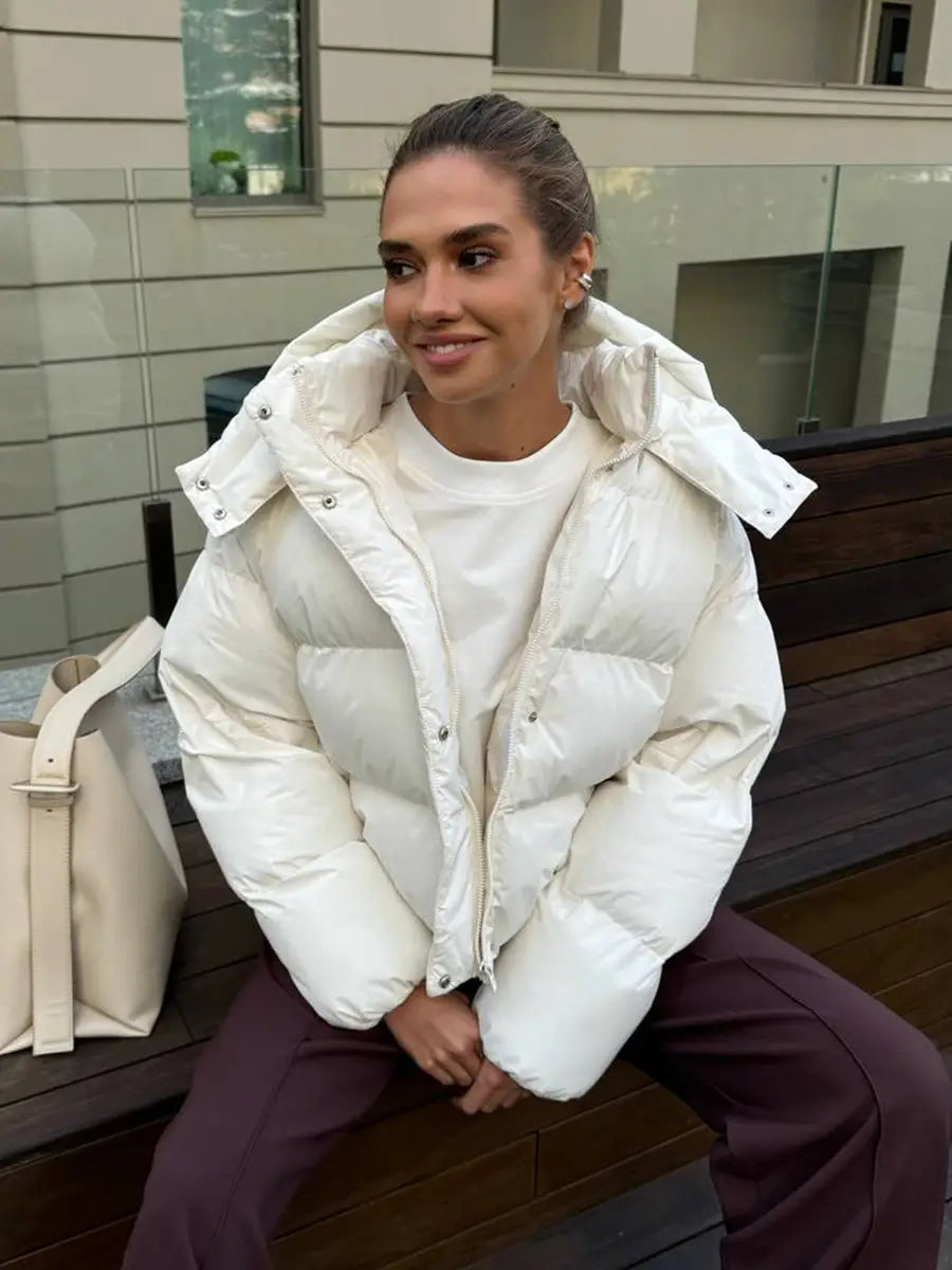 Weiße wattierte Pufferjacke mit Kapuze mit gestepptem Design und silberfarbenen Druckknöpfen für das Tragen bei kaltem Wetter.