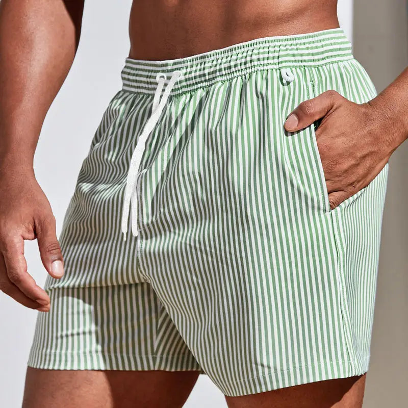 Men’s striped tropical print swim trunks featuring light green and white vertical stripes with an elastic waistband and drawstring for a comfortable fit.
