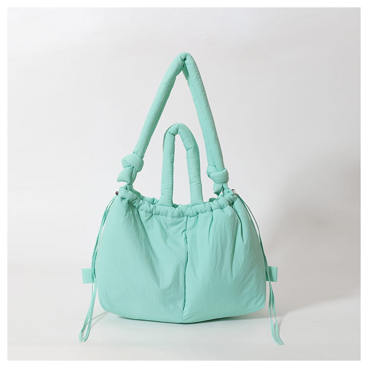 Mint green quilted puffer tote bag made of lightweight nylon featuring knotted handles and a drawstring closure for use as a shoulder bag.