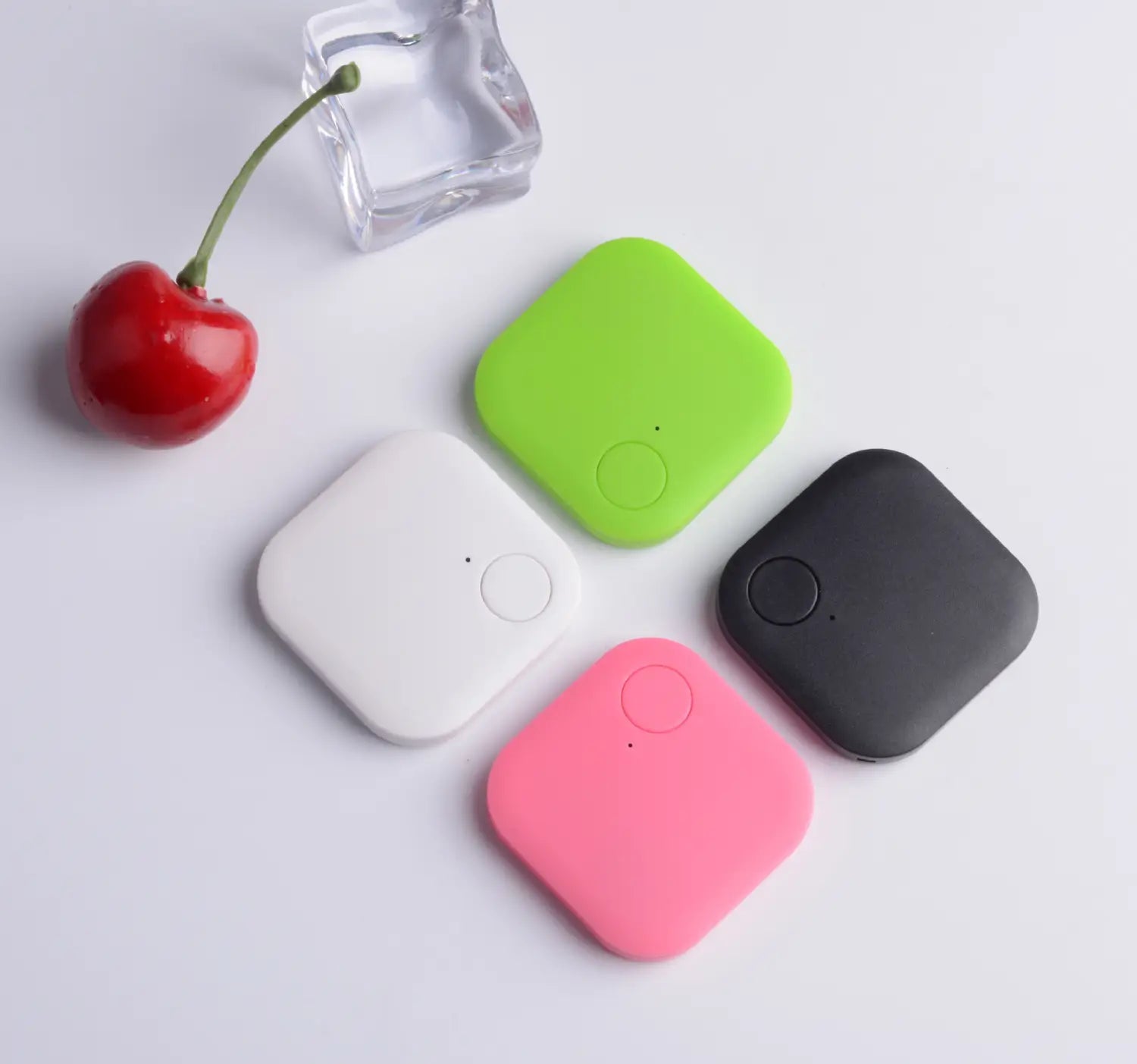 four square-shaped bluetooth tracker 4 pack anti lost gps key finders in white lime green black and pink soft-touch silicone arranged on a clean surface