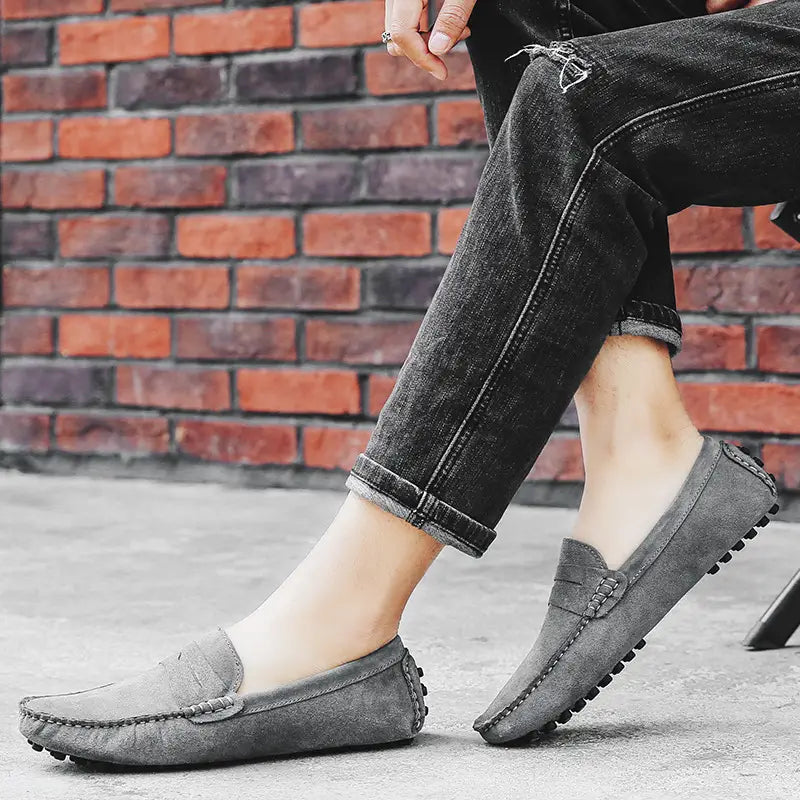 Mocassins en daim gris pour homme, avec un design cousu et des semelles en caoutchouc texturées, présentés de face.