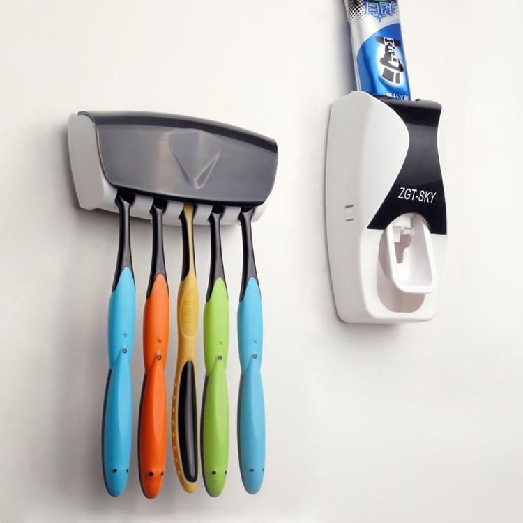 Gray and white wall-mounted automatic toothpaste dispenser and toothbrush holder set with five colorful toothbrush handles in blue orange yellow green and light blue.