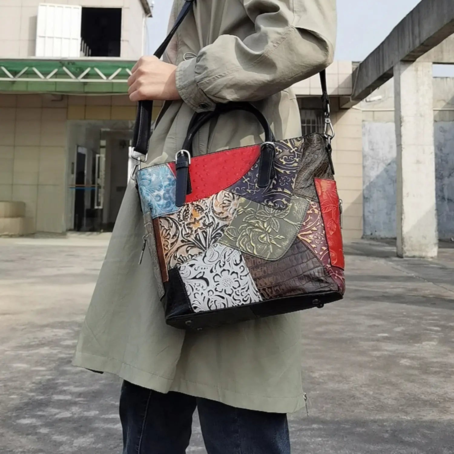 A patchwork leather women’s messenger shoulder bag with vibrant red blue and black sections and intricate floral embroidery on a textured surface.