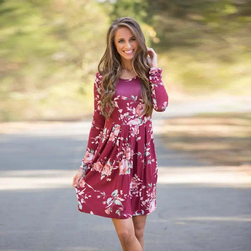 Robe midi évasée de type A, à manches longues, à imprimé floral, taille haute, bordeaux profond, avec des fleurs rose tendre et blanches, réalisée dans un tissu léger et fluide.