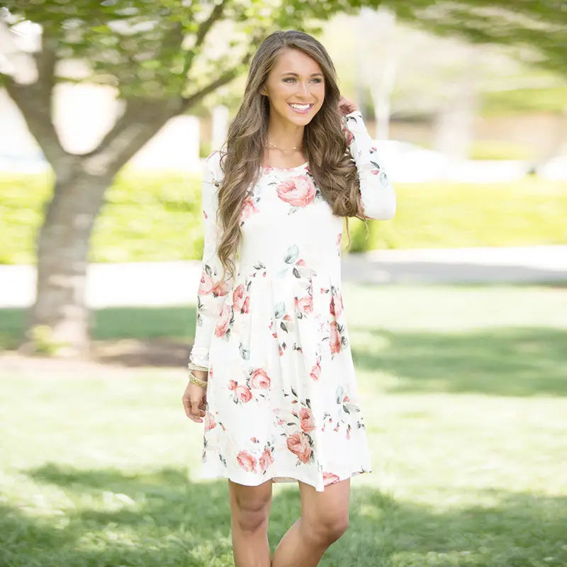 Une femme porte une robe midi évasée de type A, à manches longues, à imprimé floral, taille haute, blanche, avec des motifs rose et vert.