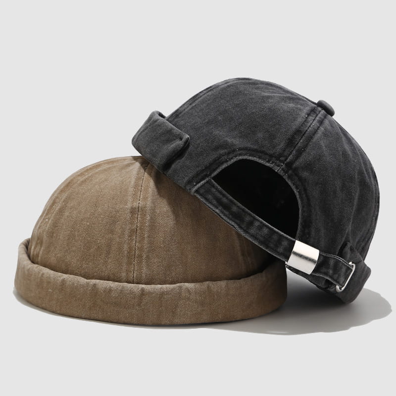 Dark gray washed denim baseball cap with a silver buckle and rolled brim resting atop a tan washed denim baseball cap.