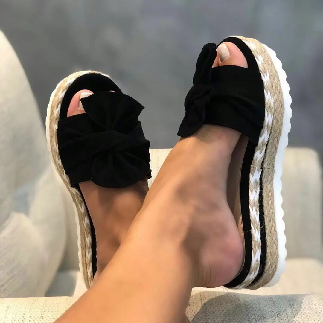 Women platform bow espadrille slide sandals featuring black fabric bows with woven jute soles and white rubber edges.