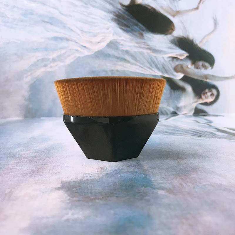 A sleek black hexagonal handle foundation brush with a dense golden brown bristle head from a powder makeup set with case.