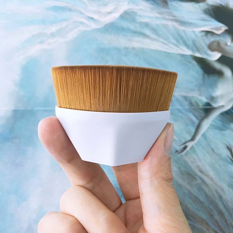 A compact foundation brush with a white plastic handle and dense golden-brown synthetic bristles from a foundation brush and powder makeup set with case.