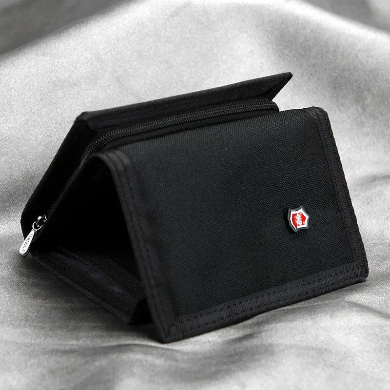 Cartera táctica de lona negra tipo billetera plegable en tres con un emblema de logotipo rojo y plateado en el frente, diseñada para guardar monedas.