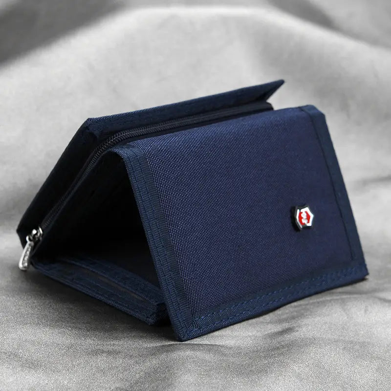 Cartera de lona de tela tejida azul oscuro con un logotipo en forma de escudo rojo y blanco en el frente, diseñada como portamonedas táctico plegable en tres.
