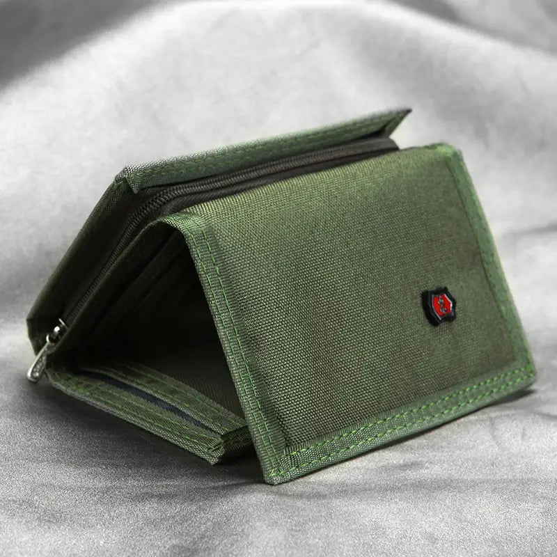 Cartera de lona color verde oliva con un emblema de escudo rojo y negro, diseñada como portamonedas táctico plegable en tres.