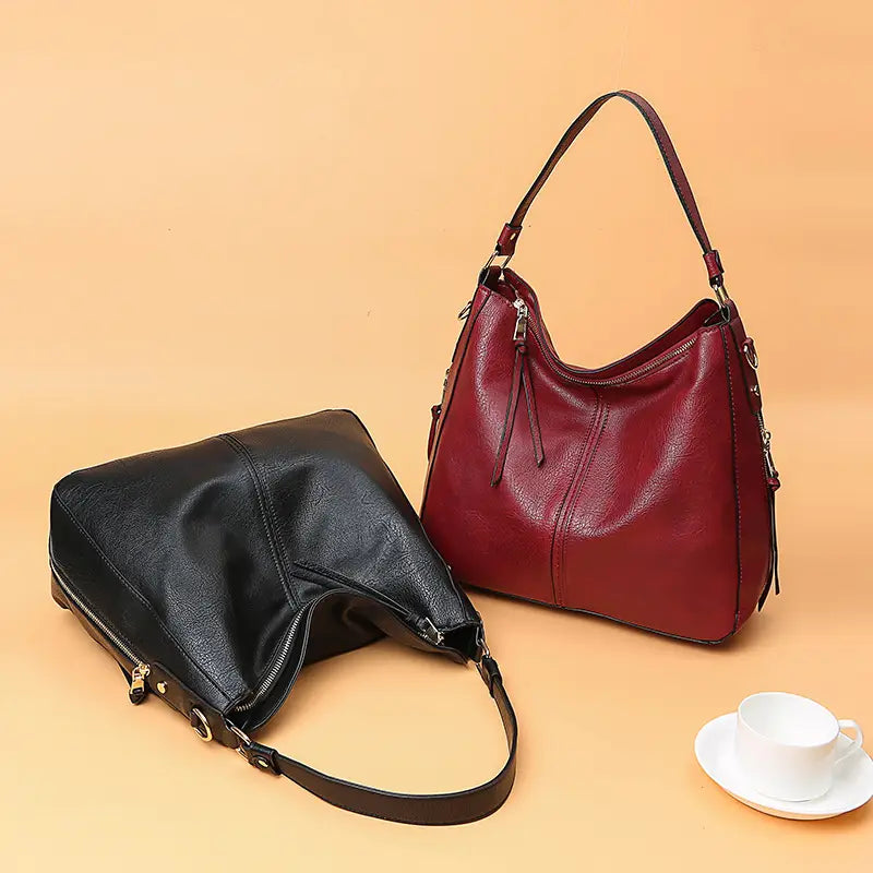 A sleek black and rich burgundy large capacity faux leather zippered hobo shoulder bag with adjustable straps.