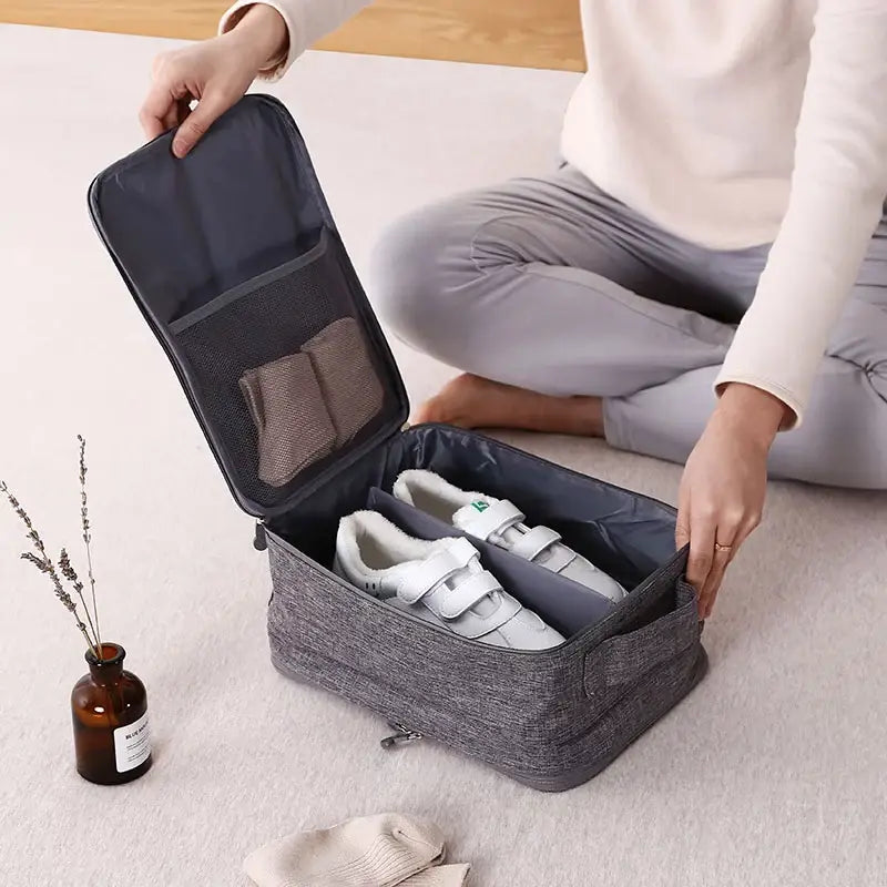 Housse de rangement pour chaussures en tissu gris texturé, avec intérieur en mesh et compartiments zippés pour organiser efficacement les bagages de voyage portables.