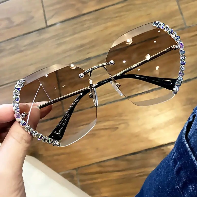 Stylish brown-tinted aviator sunglasses with a sleek metallic frame adorned with sparkling rhinestones along the edges featuring a diamond studded rimless polygonal gradient design.