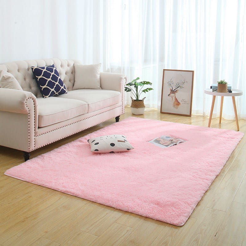 Alfombra shaggy esponjosa de color rosa suave, hecha de pelo sintético suave con una textura esponjosa, colocada sobre un suelo de madera clara y lavable a máquina.