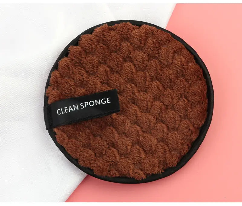makeup removing puff 3 pack featuring a brown plush textured circular cleaning sponge with a black border and a clean sponge label in a mesh bag.