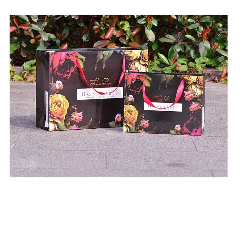 Two elegant black paper shopping bags with vibrant floral patterns and red handles, accompanying the 3d wooden steam locomotive puzzle model kit.