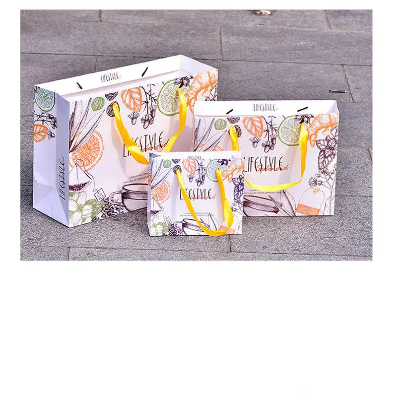 three white paper shopping bags with vibrant yellow handles and a colorful illustration of citrus slices herbs and tea elements accompanying a 3d wooden steam locomotive puzzle model kit
