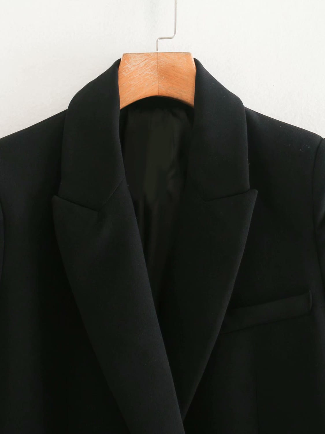 Black wool women’s tailored double breasted longline blazer coat with notched lapels hanging on a wooden hanger.
