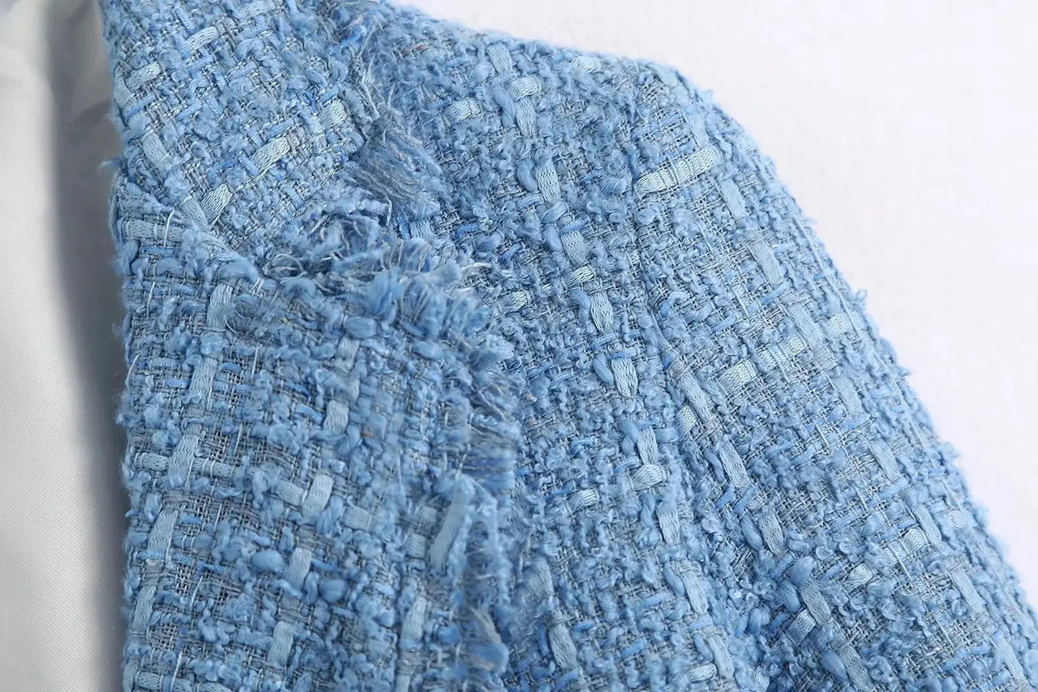 Women’s double breasted light blue textured tweed blazer fabric with a woven pattern and frayed edges.