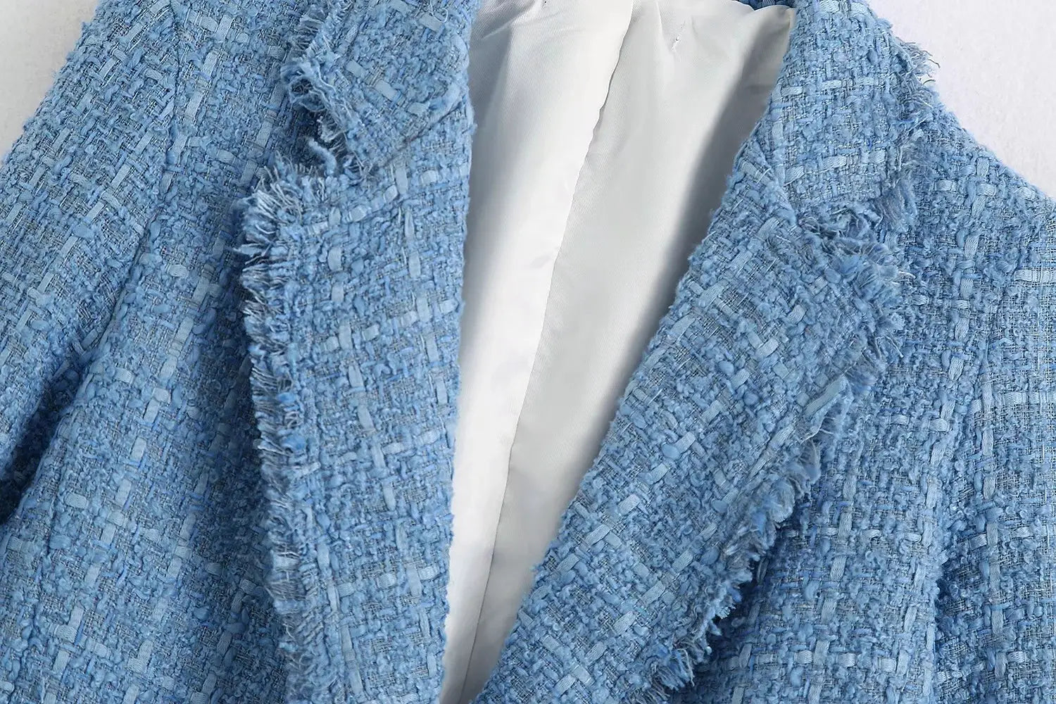Women’s double breasted light blue textured tweed blazer with a frayed hem and white lining.