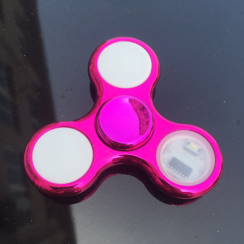 Led fidget spinner glow in dark metallic hand toy in vibrant pink with three white circular sections and a central glowing purple hub.