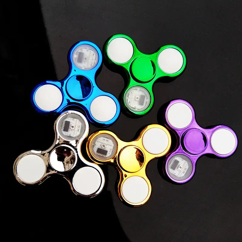 led fidget spinner glow in dark metallic hand toy featuring colorful metallic arms with white circular ends and visible circuit boards inside.