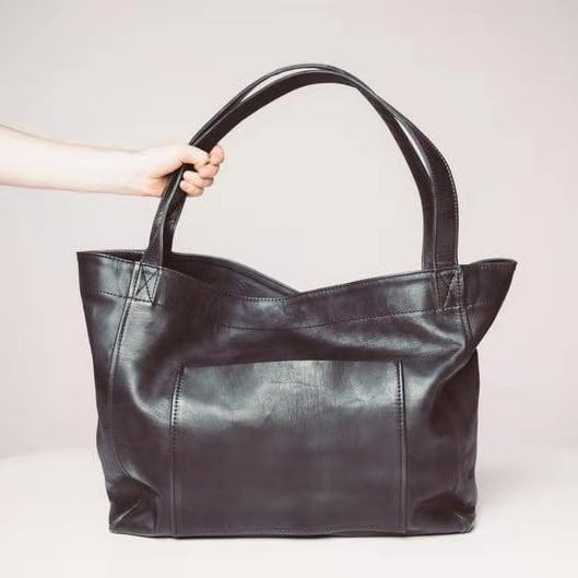 Black leather tote bag with large capacity oil wax leather material, sturdy handles, and a front pocket for shoulder use.
