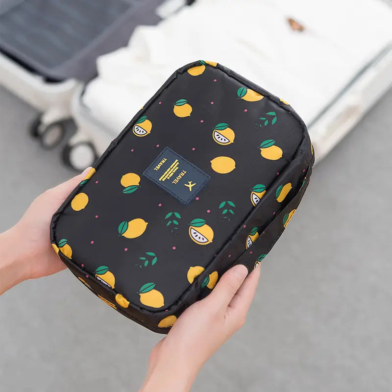 Schwarzer hängender Kulturbeutel-Organizer für Reise-Make-up mit verspieltem Gelb-Grün-Zitronenmuster und kleinem dunkelblauem Reiseetikett auf der Vorderseite.