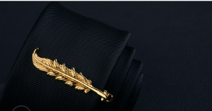 golden feather-shaped tie clip from the men’s airplane tie clip and lapel pin gift set rests elegantly on a black textured fabric surface.