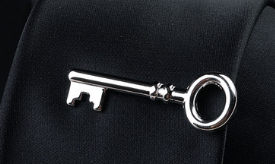 Silver key-shaped pin with polished metallic finish and ornate detailing on the bow from a men’s airplane tie clip and lapel pin gift set.