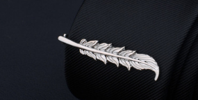 Silver feather-shaped pin with intricate detailing from the men’s airplane tie clip and lapel pin gift set made of silver metal.