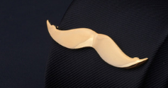 Gold-colored metallic mustache-shaped lapel pin from the men’s airplane tie clip and lapel pin gift set.