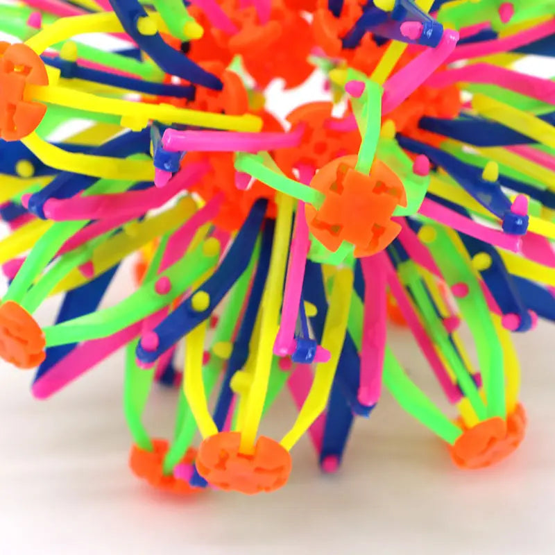 Jouet de balle magique à expansion, sphère télescopique colorée, avec une bille en plastique épineuse aux couleurs néon et des tiges flexibles orange, rose, bleues et vertes rayonnant depuis un cœur central.