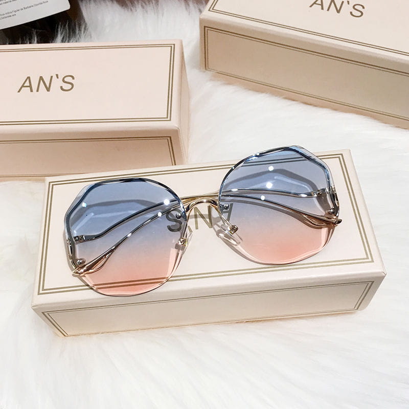 Ein Paar Sonnenbrillen mit übergroßem, geometrischem Metallrahmen im Gradient-Design, mit eleganten goldfarbenen Gestellen und Linsen, die von Blau zu Pink übergehen, auf der Markenbox präsentiert.