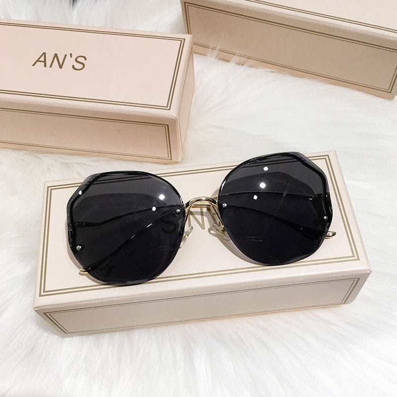 Schwarze, achteckige Sonnenbrille mit gradienten übergroßem geometrischem Metallrahmen, mit goldfarbenen Gestellen, auf einer beigen Markenbox liegend.