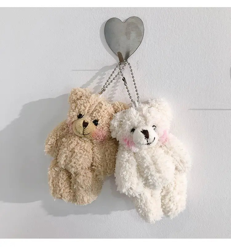 Zwei Plüsch-Teddybär-Schlüsselanhänger aus weichem beigem und flauschigem weißem Material mit bestickten Gesichtszügen und rosigen Wangen, gestaltet als niedliche Mini-Puppe-Anhängerfiguren.