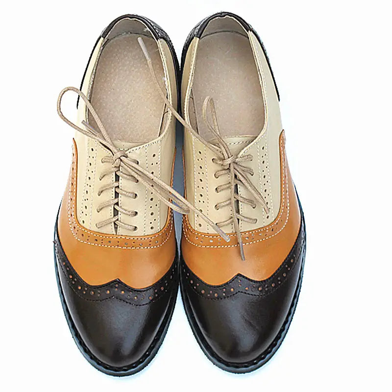 A pair of leather oxford brogue shoes womens two tone flats in tan brown and black leather with classic decorative perforations and stitching.