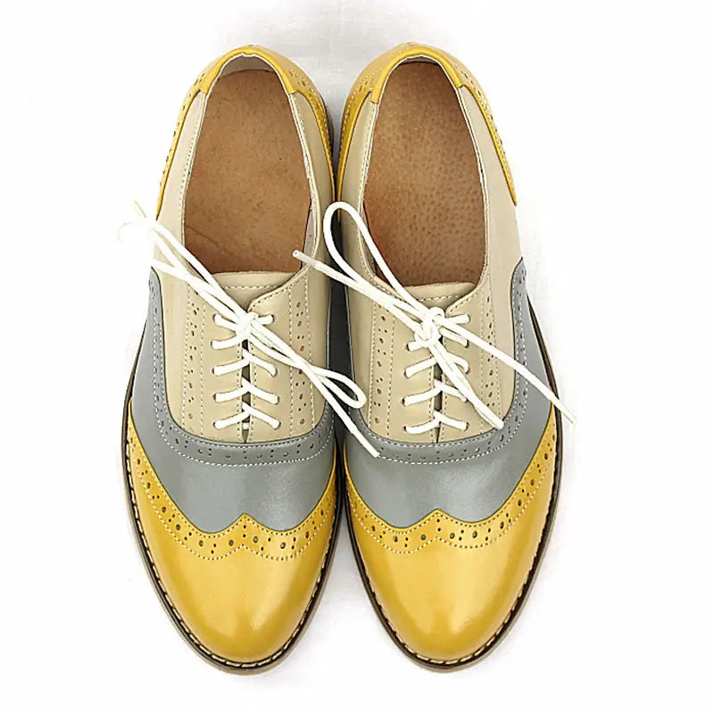 A pair of leather oxford brogue shoes for women featuring two-tone beige upper, gray side panels, and glossy mustard yellow toe caps.
