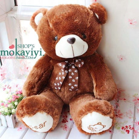 A plush teddy bear soft animal doll in brown with white accents on face paws and ears wearing a polka-dotted bow tie.