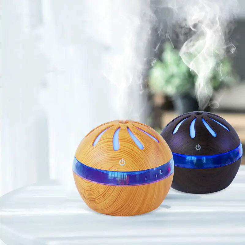 Two spherical Windmill wooden aroma diffusers with 1l capacity featuring light wood grain and dark black finishes with glowing blue led bands around their midsections.